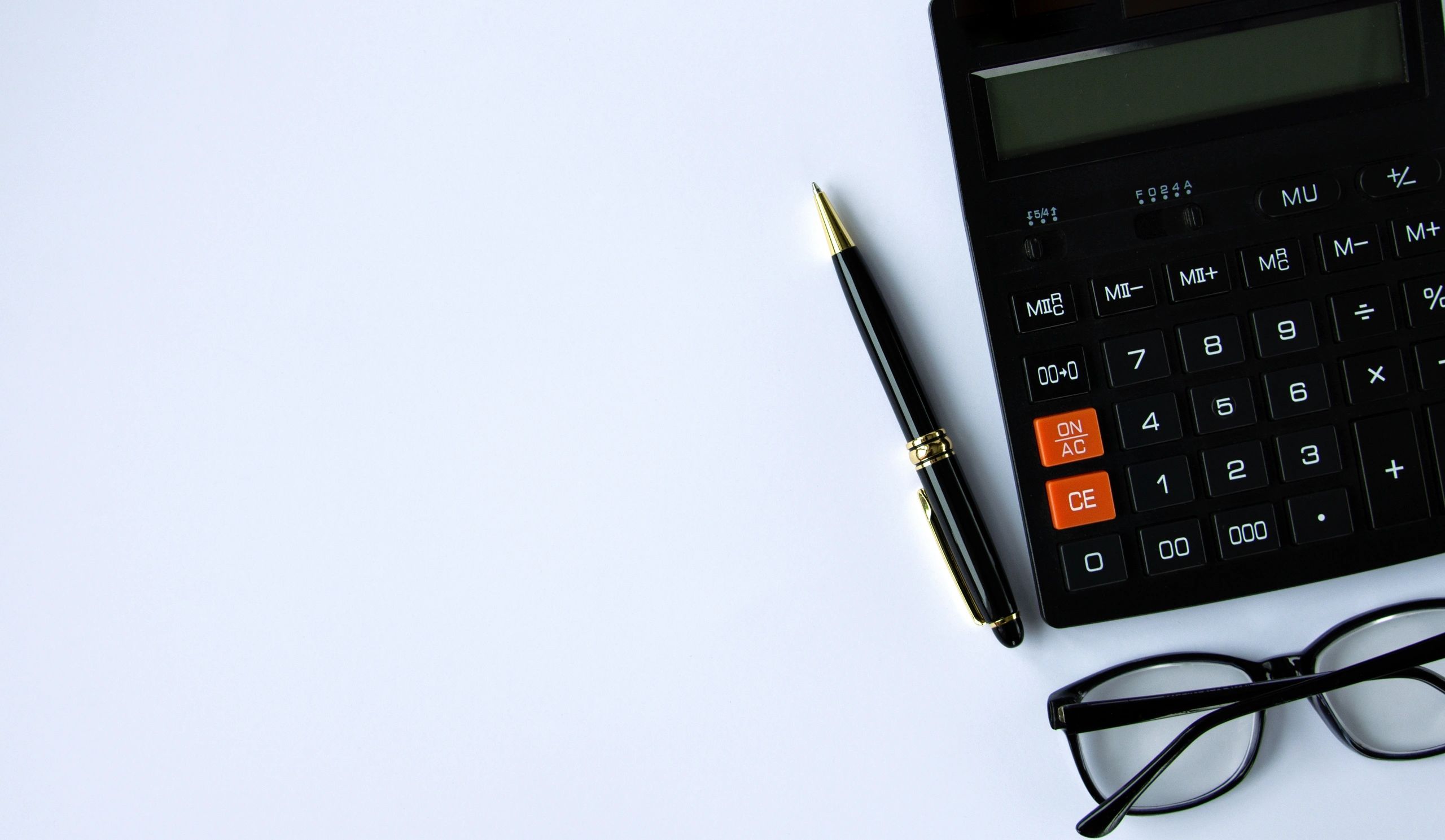 Notebook, calculator, pen and glasses arranged on a desk