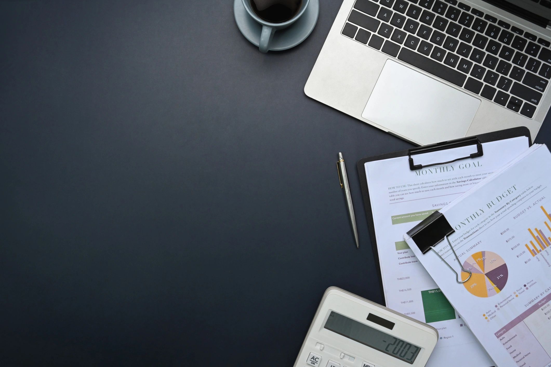 Top view of office desk with laptop, calculator, financial reports, and coffee cup